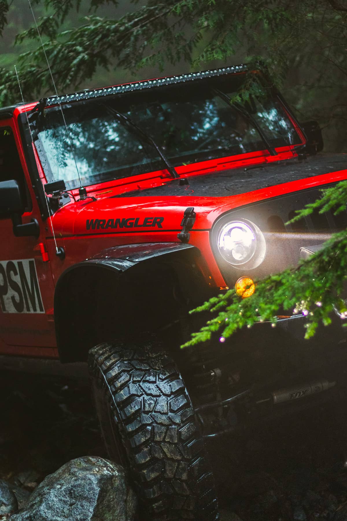 Red Jeep Wrangler with off-road mods wheeiling in the forest