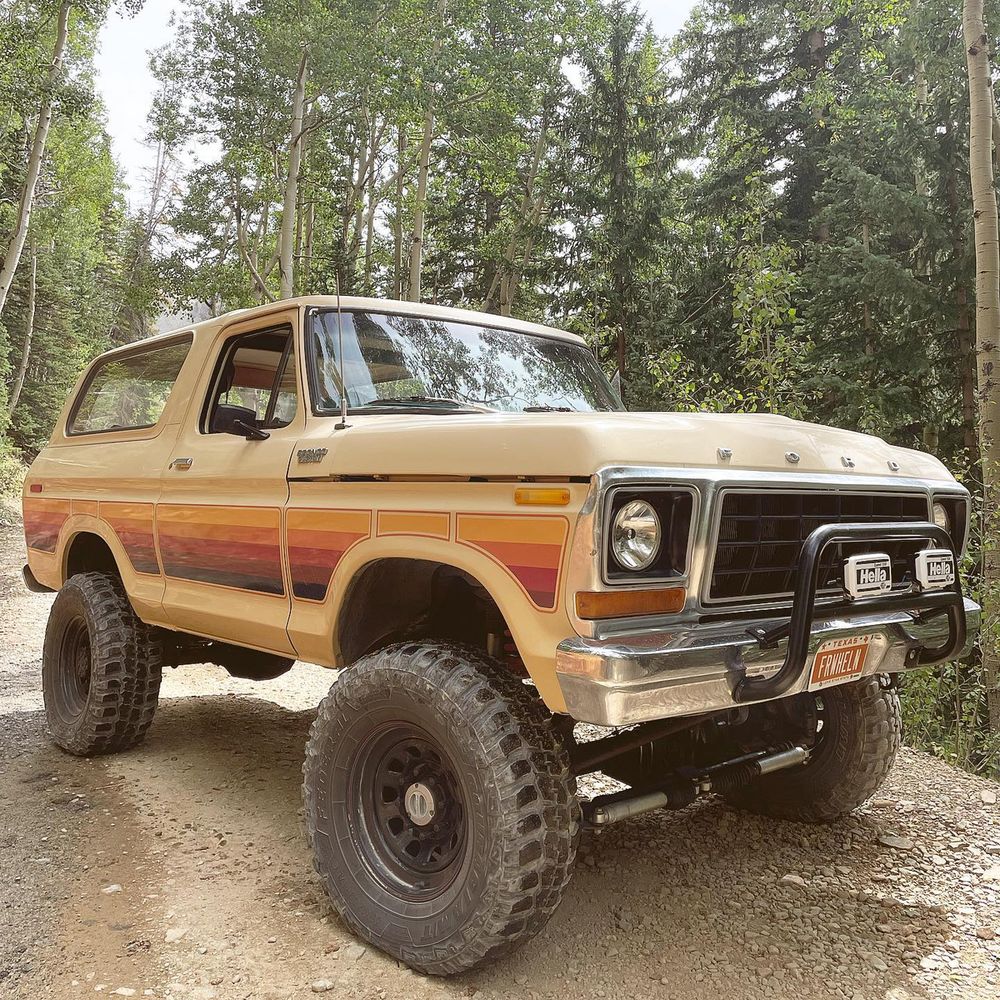 Hella auxiliary lights mounted on a brush bar of a tan lifted Ford Bronco on a forest trail