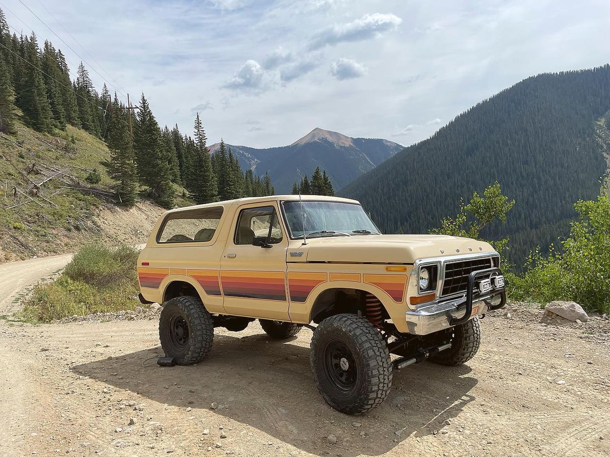 1978 Ford Bronco Custom in tan with retro stripe parked on a mountain dirt road in Colorado