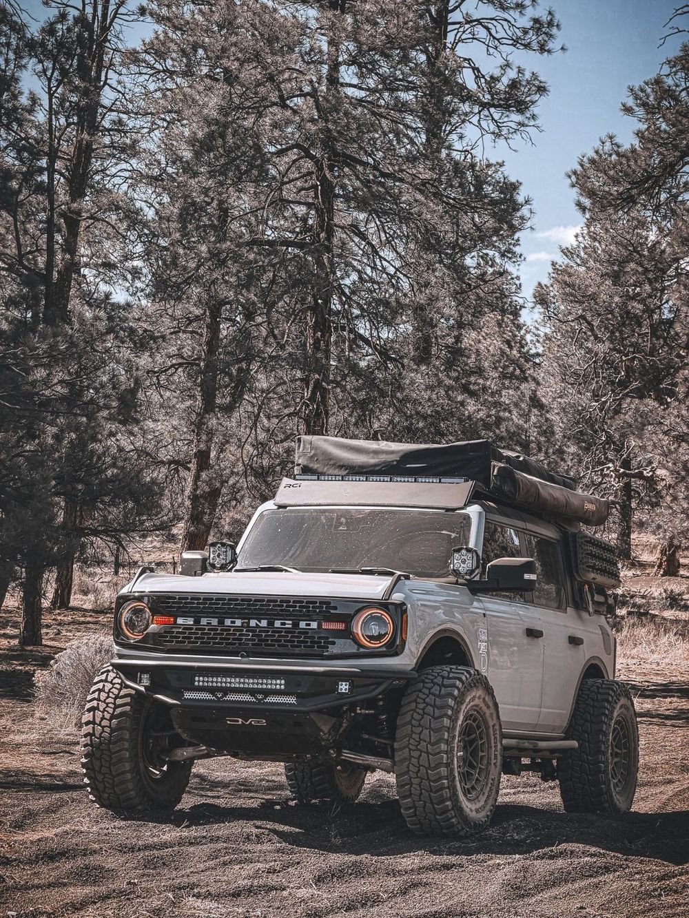2022 gray Ford Bronco Wildtrak with a rooftop tent and orange DRL headlight halos in forest