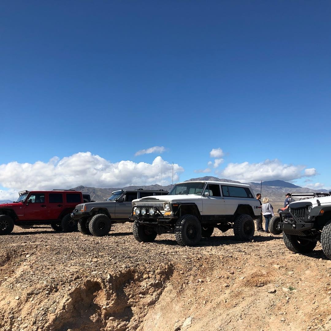 White 1978 Jeep Cherokee Chief SJ with custom tube bumpers at a desert offroad meetup
