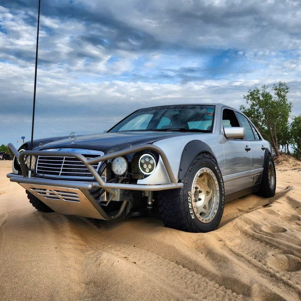 Beadlock wheels on a lifted silver Mercedes W210 prerunner parked on sand