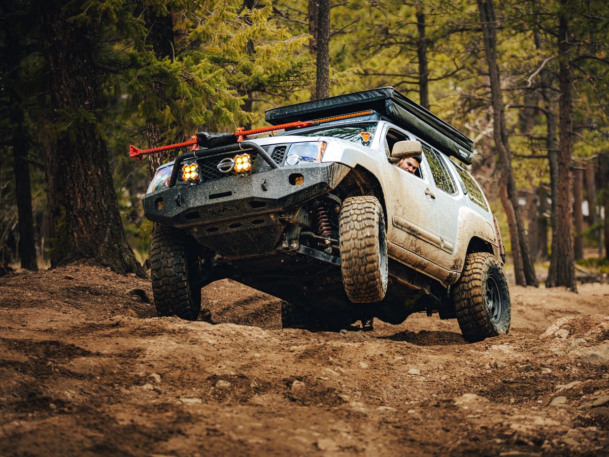 Silver 2nd Gen Nissan Xterra with Fox 2.0 Titan Swap coilovers visible on a muddy forest trail