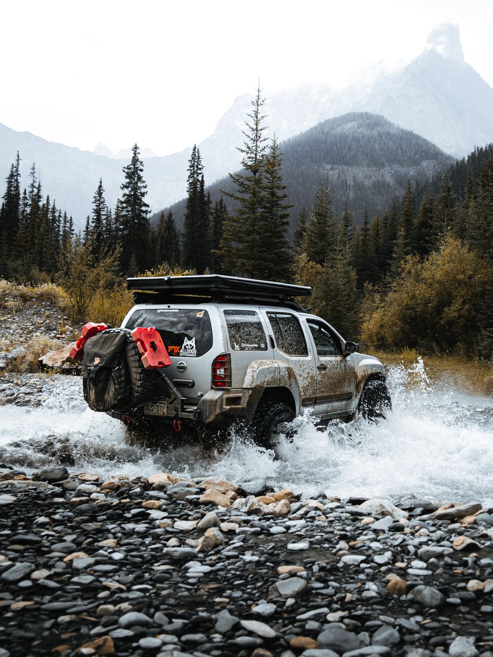 Silver Nissan Xterra crossing a rocky river with red Maxtrax recovery boards mounted on the rear