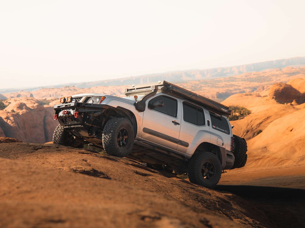 Silver 2nd Gen Nissan Xterra climbing steep Moab slickrock showing Z1 Offroad ATK-06 wheels