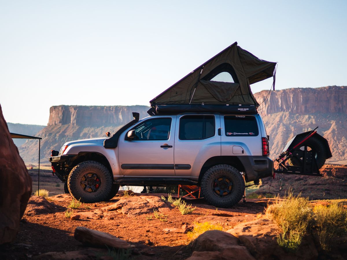 Nissan Xterra with rooftop tent fully deployed while camping on Moab red rock at dusk