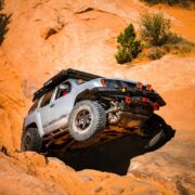 Lifted silver Nissan Xterra descending a steep Moab rock face showing CJD Racing shackles