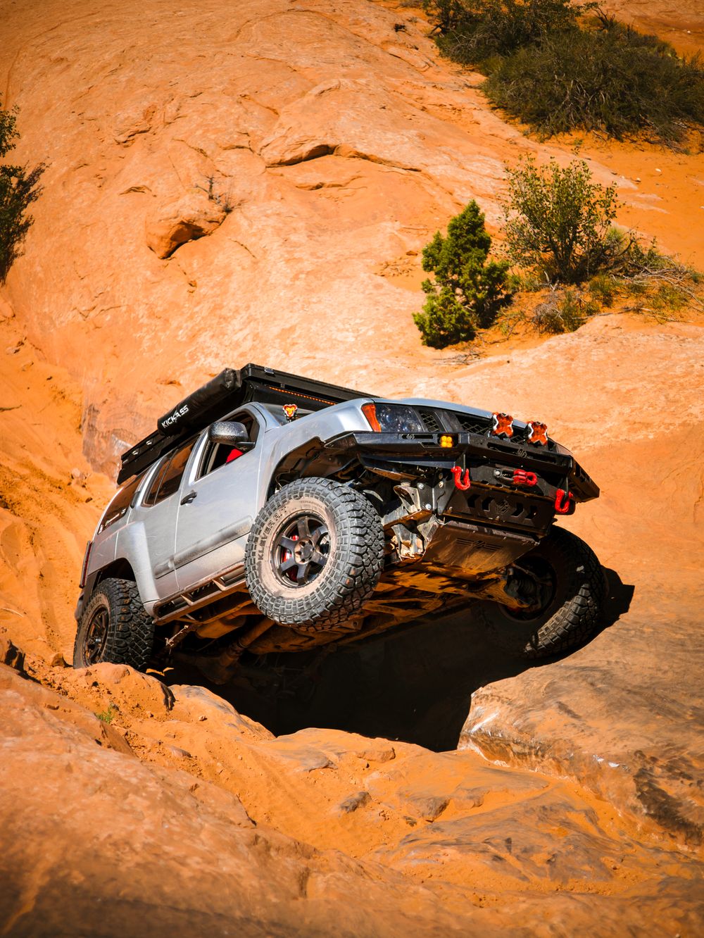 Lifted silver Nissan Xterra descending a steep Moab rock face showing CJD Racing shackles