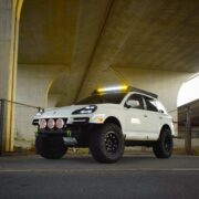 White 957 Porsche Cayenne with STEDI off-road lights on a custom front bumper under a bridge