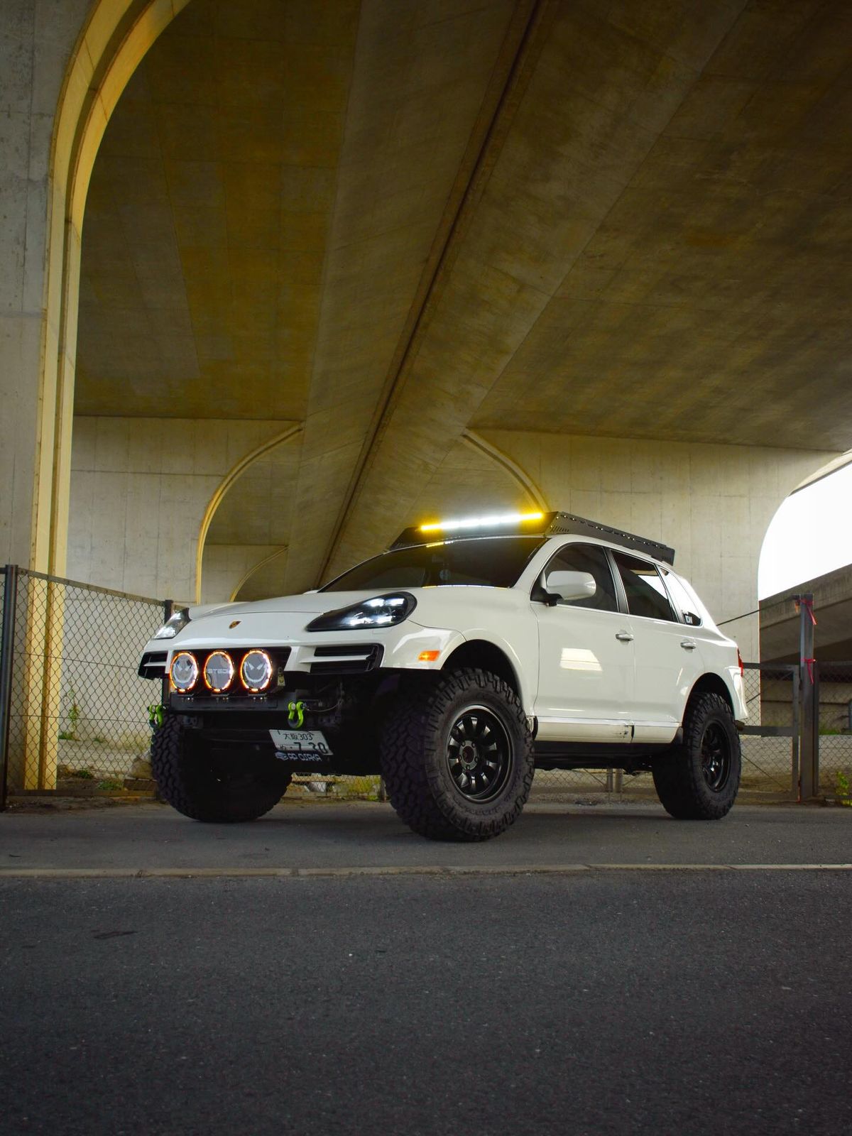 White 957 Porsche Cayenne with STEDI off-road lights on a custom front bumper under a bridge