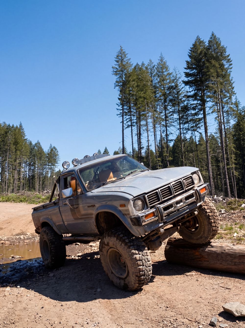 Lifted Toyota Hilux pickup flexing over a log obstacle showing Fox 2.0 reservoir shocks
