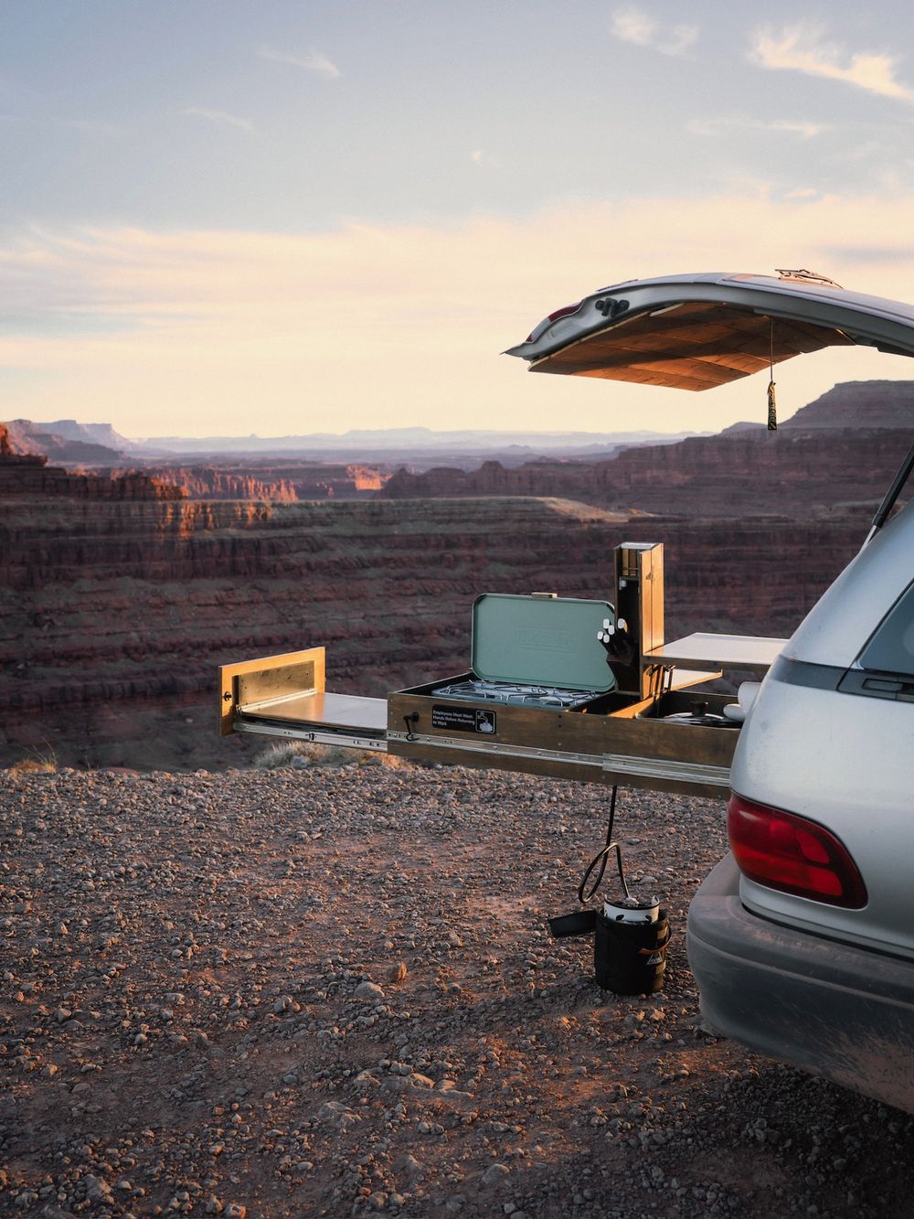 Pull-out camp kitchen extended from the rear of a Toyota Previa overlooking a canyon at sunset