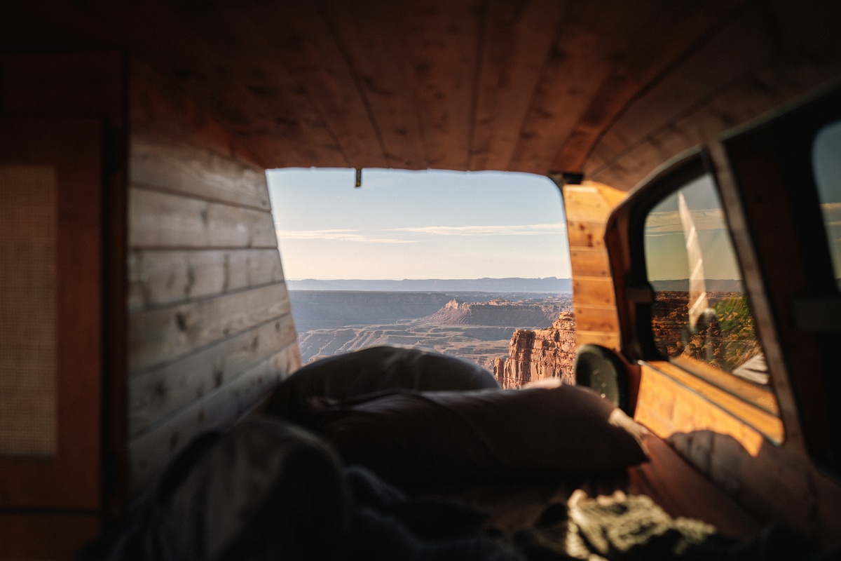 Twin bed inside a Toyota Previa camper conversion with a canyon view through the rear window