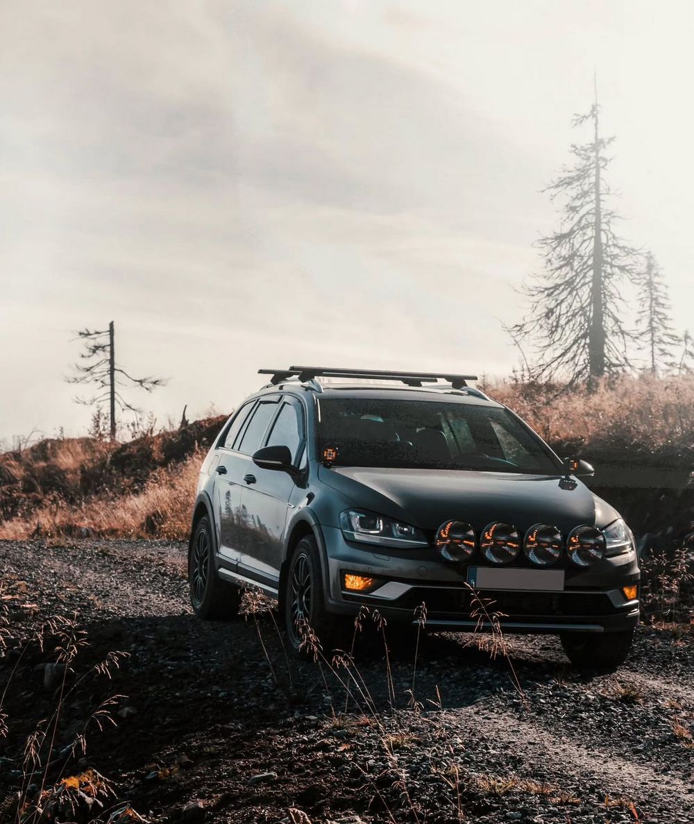Lifted VW Golf Alltrack wagon with roof rack and rally lights positioned on rugged off-road terrain