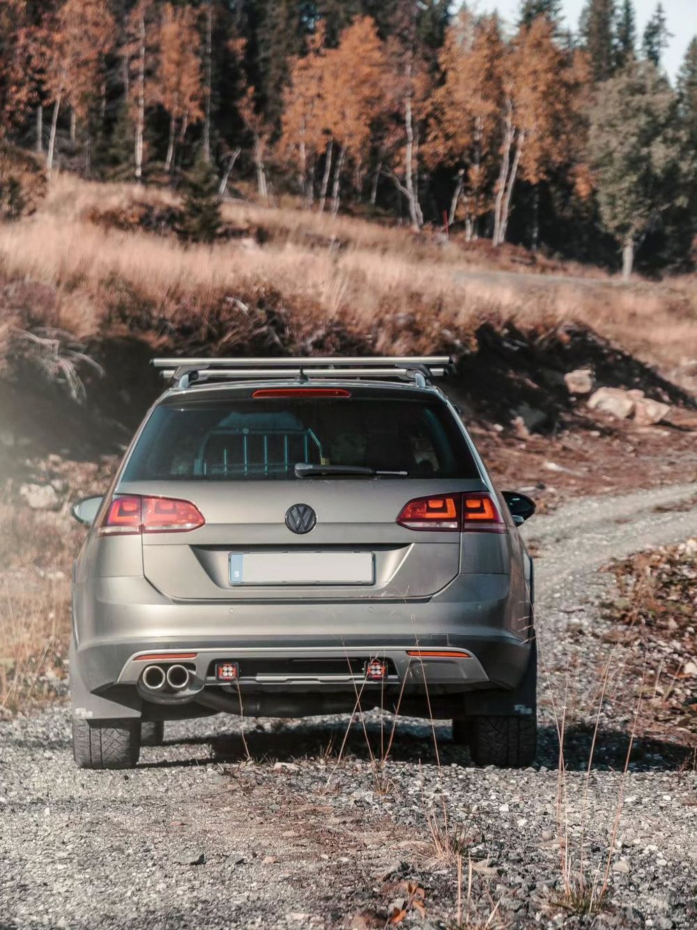 Lifted VW Golf Alltrack wagon with roof rack and Friedrich Motorsport exhaust on gravel trail in autumn forest